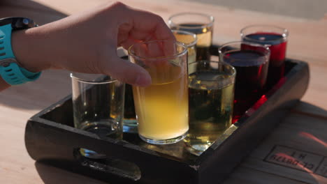 closeup shot of a hand grabbing a glass from a flight of hard cider