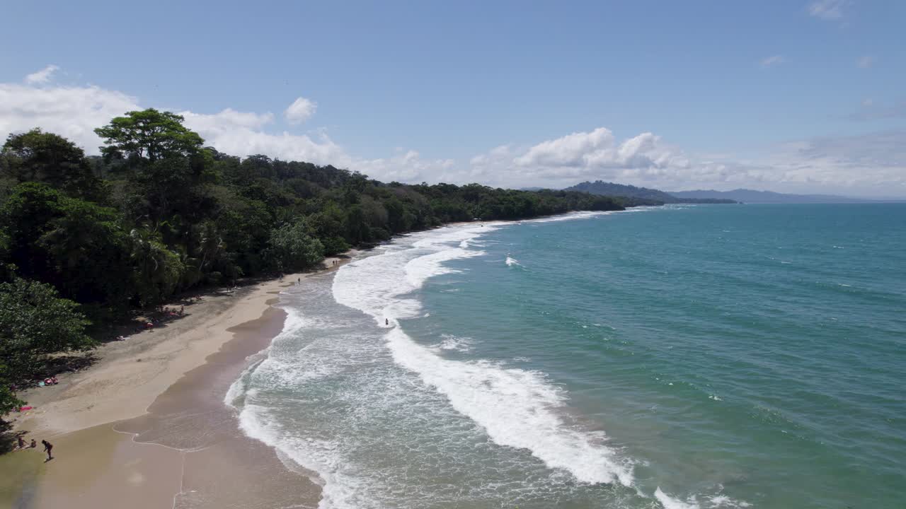 Vista aérea de una escena de playa tropical en Punta Uva, con un exuberante bosque verde bordeando la costa y suaves olas azules del océano.