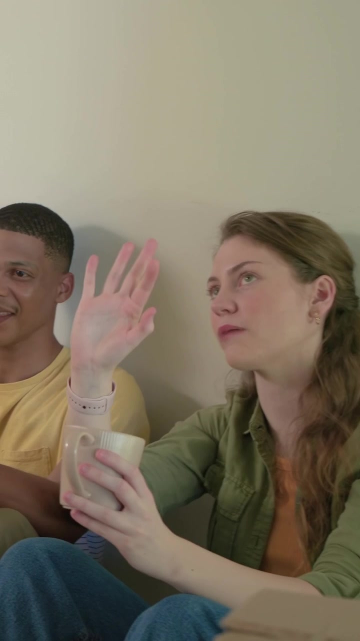 Vertical video: Door opening, woman in green top holding mug touching man at home, moving with box