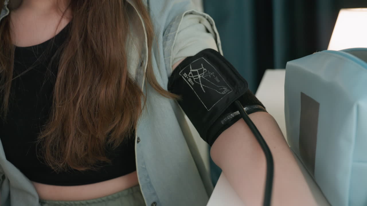 Giovane donna caucasica che controlla un monitor digitale con viso concentrato e bracciale visibile sul braccio, un ritratto ravvicinato cattura un'espressione introspettiva, che si protende verso il display del dispositivo e preme un pulsante