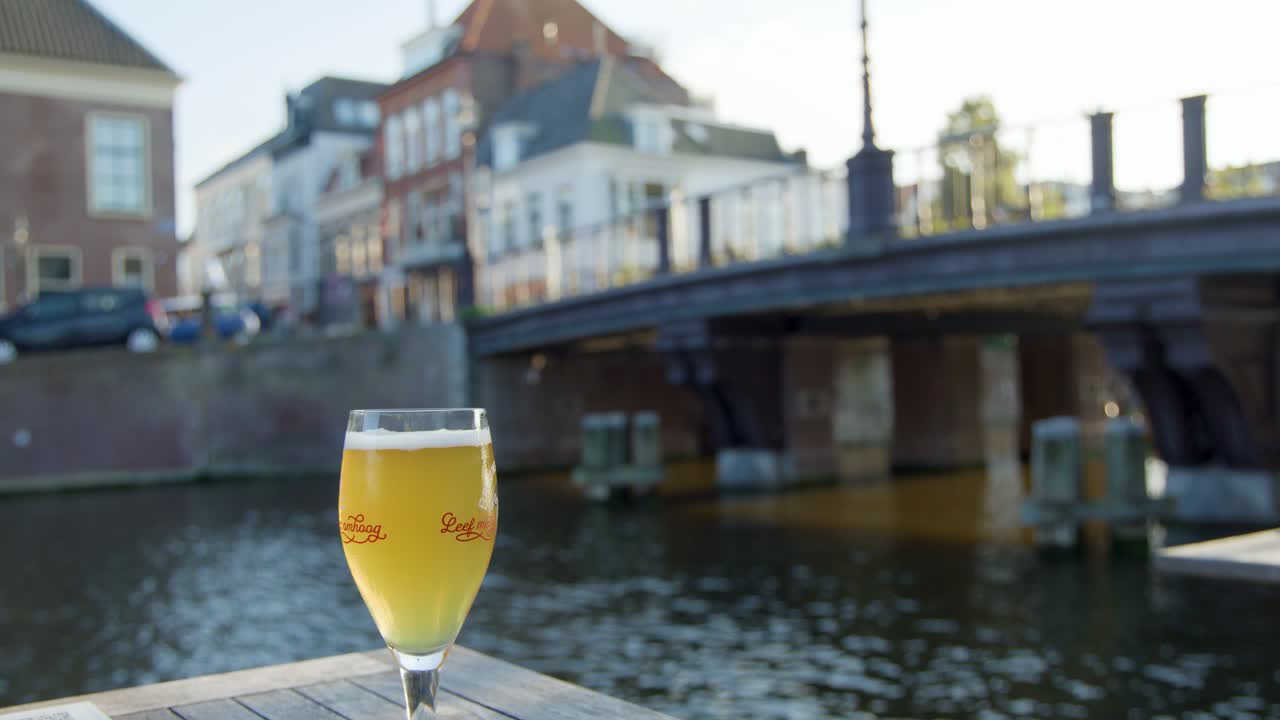 Hand lifts beer glass from outdoor table by canal in Haarlem, Netherlands, with soft daylight
