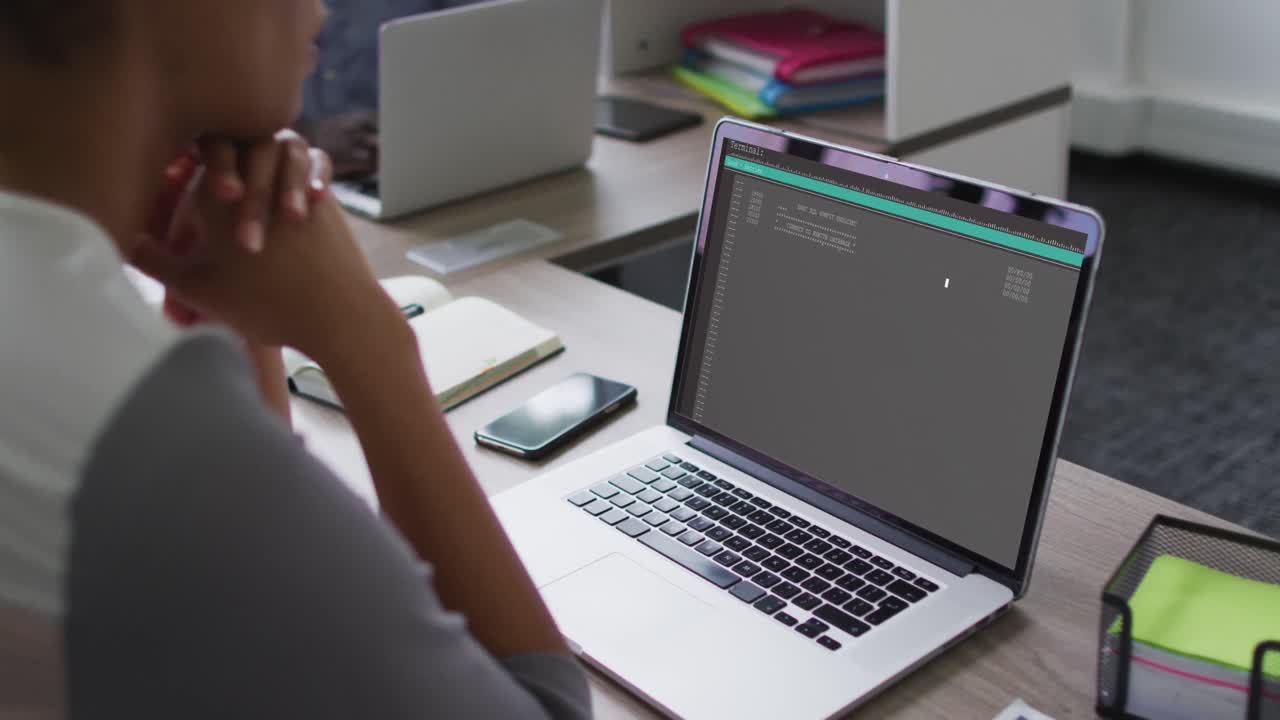 Mixed race woman sitting at desk watching coding data processing on laptop screen