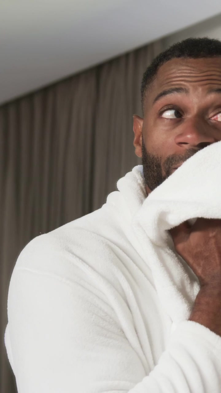 Vertical video: Lifting white towel, mature man in robe pressing it to face in bedroom drying skin