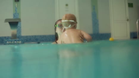 cute blonde toddler is diving under the water while his mother is holding him. his mother is teaching him how to swim. an underwater shot