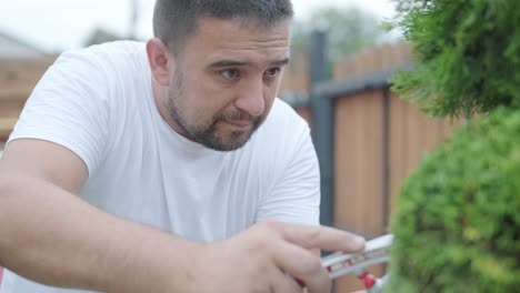 un jardinero poda arbustos decorativos con tijeras en un patio ajardinado, centrándose en la formación de plantas y la estética del jardín. valla de madera y césped verde en el fondo