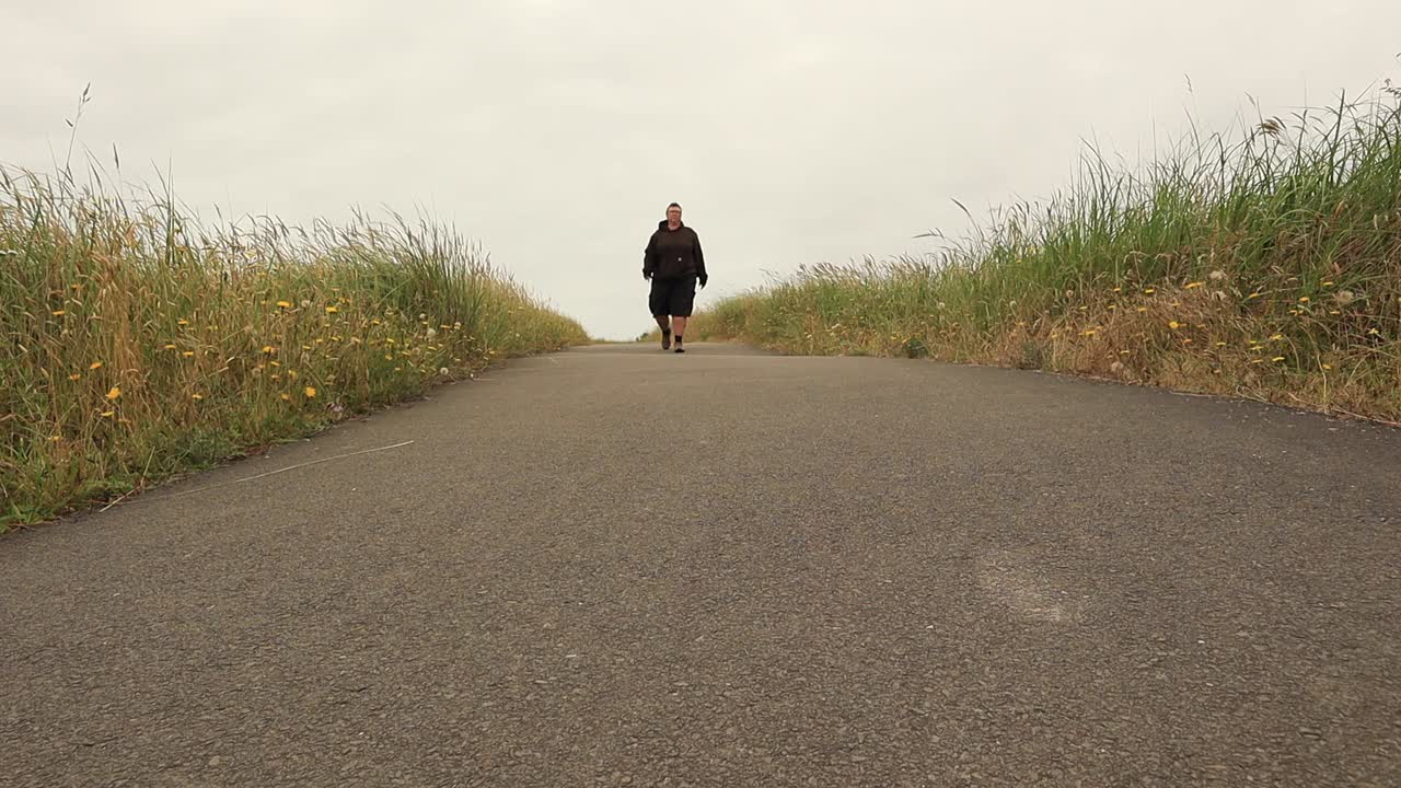 Female person walking on footpath between fields during cloudy day,low angle wide shot
