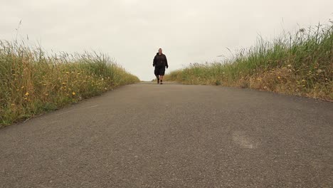 female person walking on footpath between fields during cloudy day,low angle wide shot