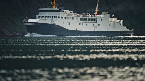 a passenger ferry sails through the calm waters of geiranger fjord, with steep cliffs rising in the background.