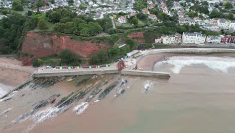 Revelación-Aérea-De-Drones-Del-Monte-Lea,-La-Colina-De-Teignmouth,-Dawlish-Con-Cabañas-De-Playa-Y-Muelle-Mientras-Un-Tren-Sale-Del-Túnel