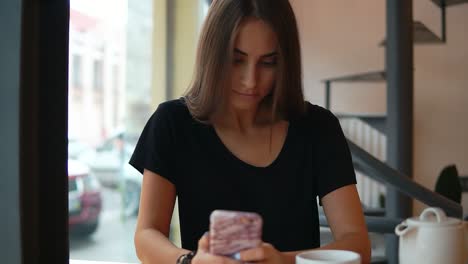 Joven-Concentrada-Con-Cabello-Largo-Y-Maquillaje-Natural-Usando-Su-Teléfono-Móvil-En-La-Toma-De-Café.-Uso-De-Dispositivos-Modernos