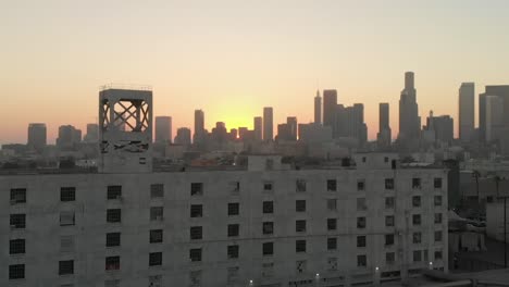 drone rising up over the city and industrial buildings with the sun setting in the background sillhouetting the skyscrapers in the distance