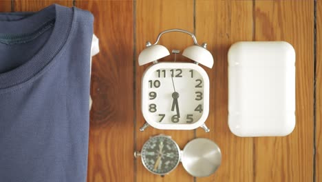 hand placing retro alarm clock among travel belongings on wood table