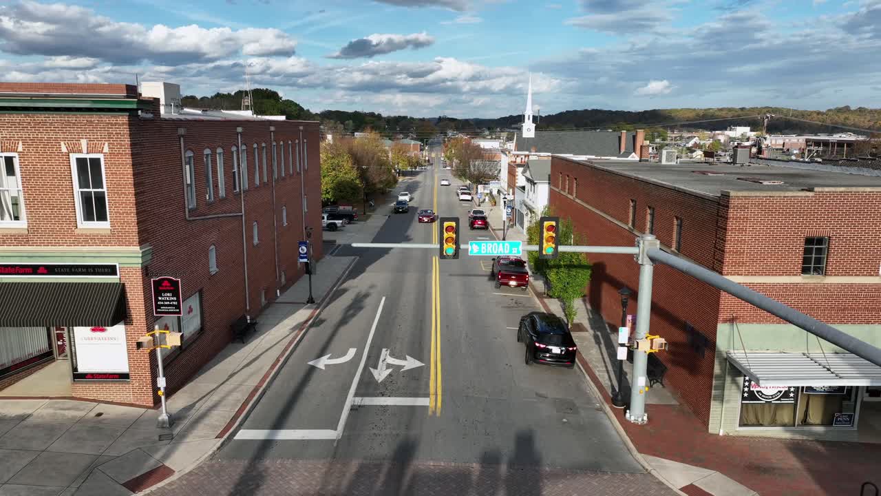 Aerial flyover main street of american town with church and red brick buildings. Sunny day in autumn season with colorful trees. Slow forward shot.