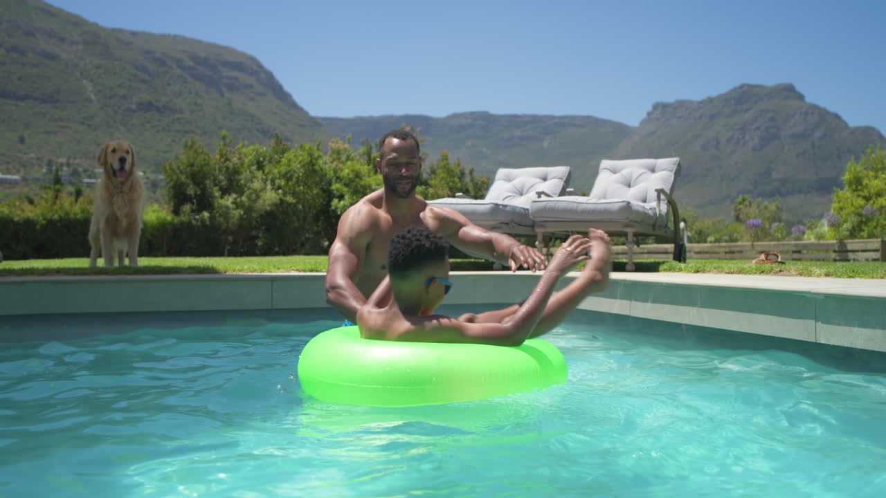 Father and son in home pool, father entering, reaching, spinning green float, playing son in shades