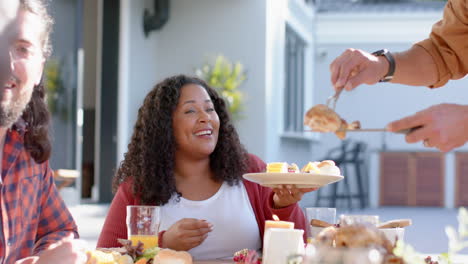 happy diverse male and female friends serving thanksgiving celebration meal in sunny garden