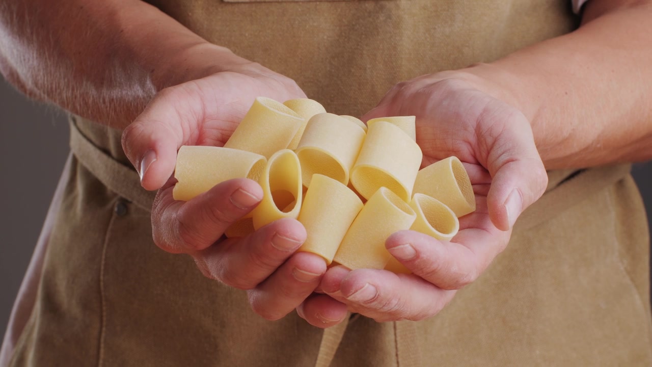Mani dello chef che tengono paccheri italiani crudi