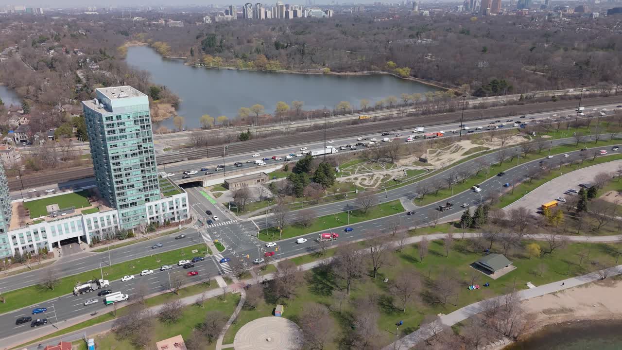 Road traffic by lake with Toronto towers in background, aerial push-in