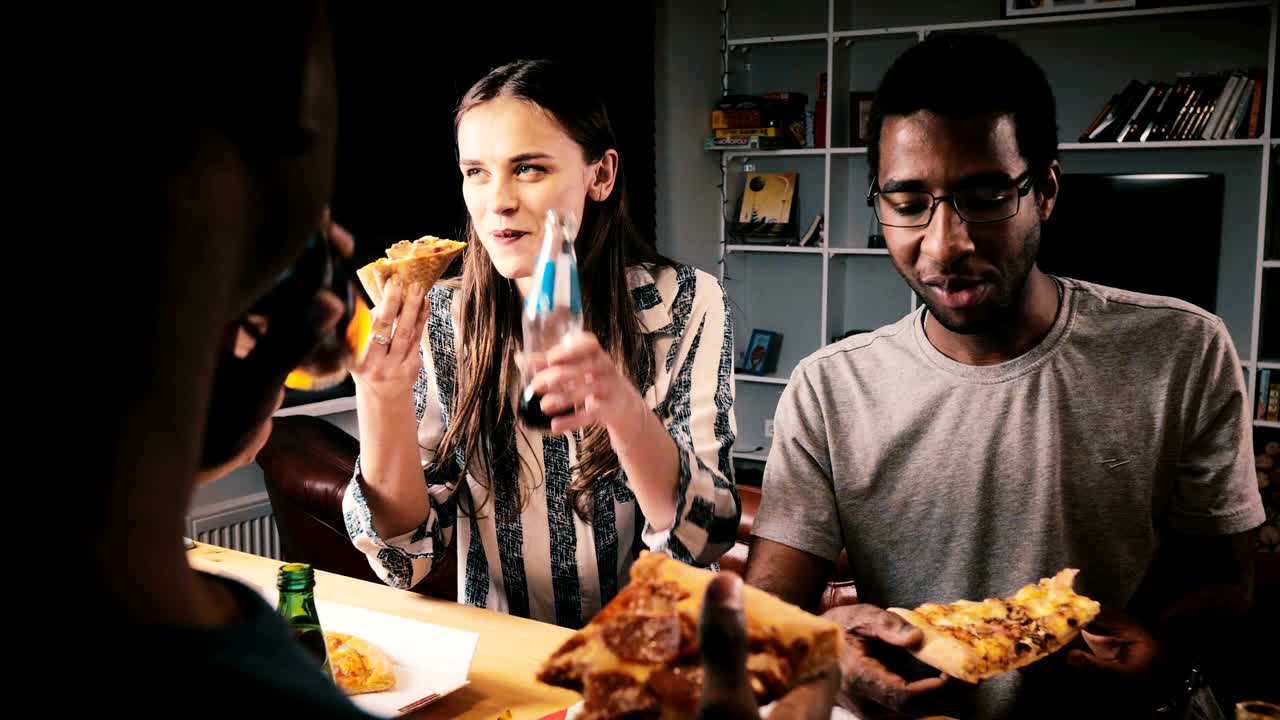 Mixed ethnicity group of happy young friends eating pizza and having drinks at a casual house party by kitchen bar table