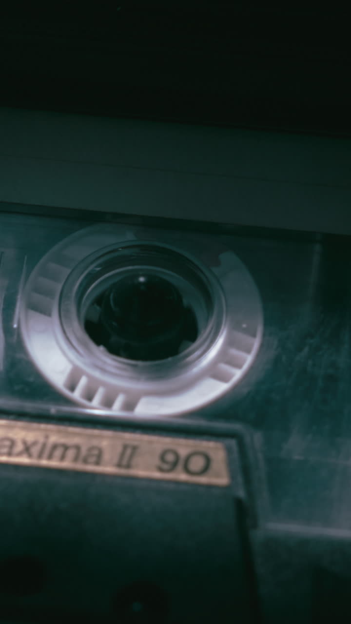 Gros plan vertical d'une cassette analogique tournant en basse lumière. Scène médiatique atmosphérique idéale pour les histoires criminelles, les interviews, les archives ou les enquêtes