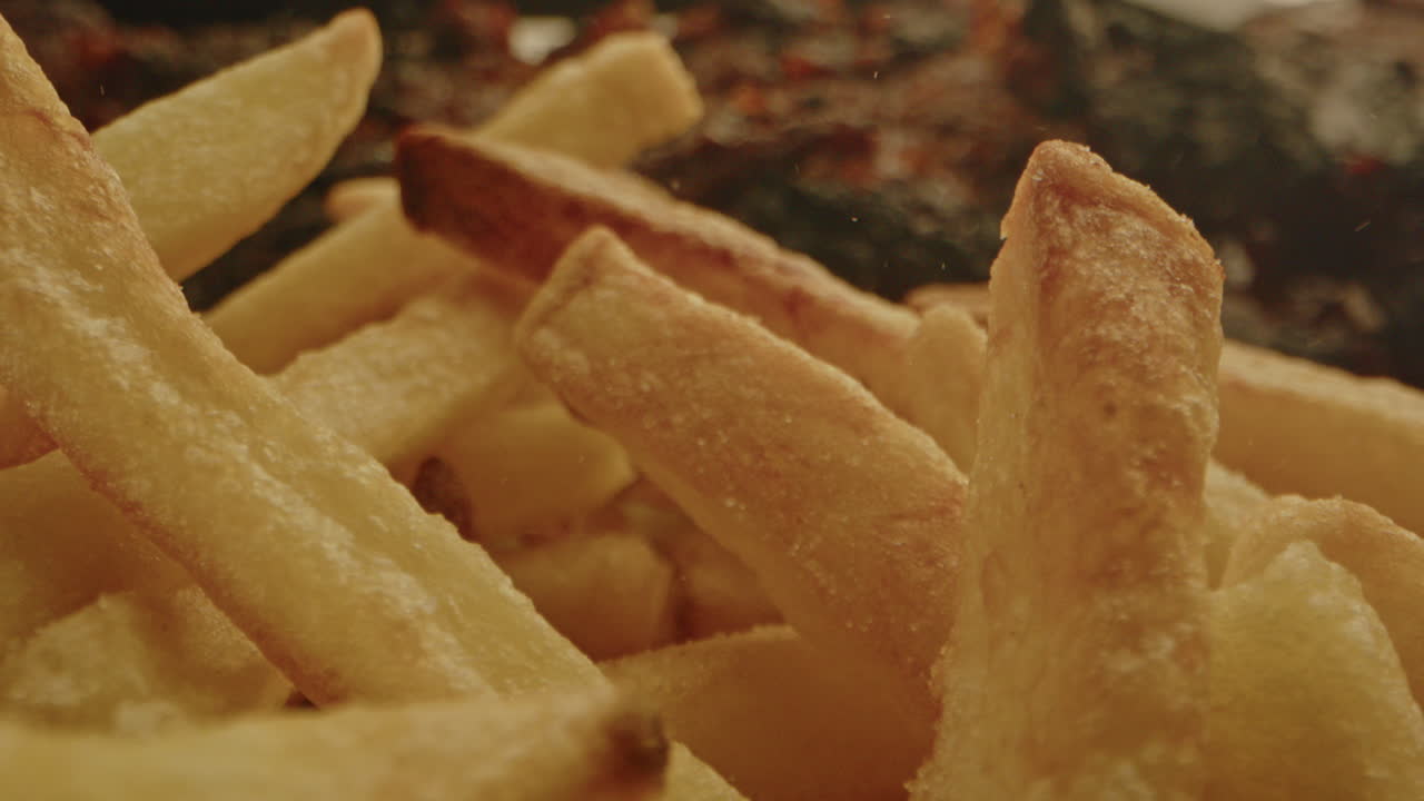 Beautiful macro of freshly baked french fries being sprinkled with salt in slow motion