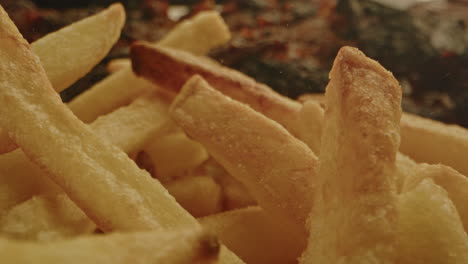 beautiful macro of freshly baked french fries being sprinkled with salt in slow motion