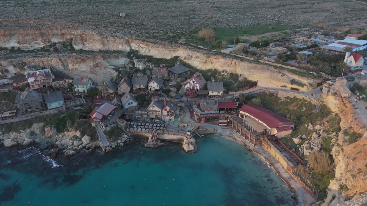 Aerial Establishing fly Popeye Village Malta Mediterranean Sea village houses next to the beach, rural countryside background