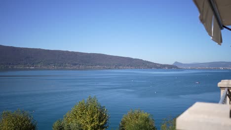 Lago-Annecy-Desde-El-Balcón-Del-Hotel-En-Un-Día-Claro-Y-Soleado-En-Los-Alpes-Franceses,-Toma-Panorámica-Hacia-La-Derecha