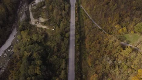 Vista-Aérea-De-Una-Carretera-Rural-Junto-Al-Río-A-Través-Del-Bosque-De-Las-Montañas-De-Los-Apeninos,-Italia