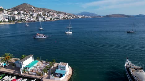 Los-Barcos-Turísticos-Entran-Con-Gracia-En-El-Tranquilo-Puerto-Costero-De-Saranda,-Entre-Barcos-Y-Paseo-Marítimo,-Perfecto-Para-Unas-Vacaciones-En-La-Ciudad.