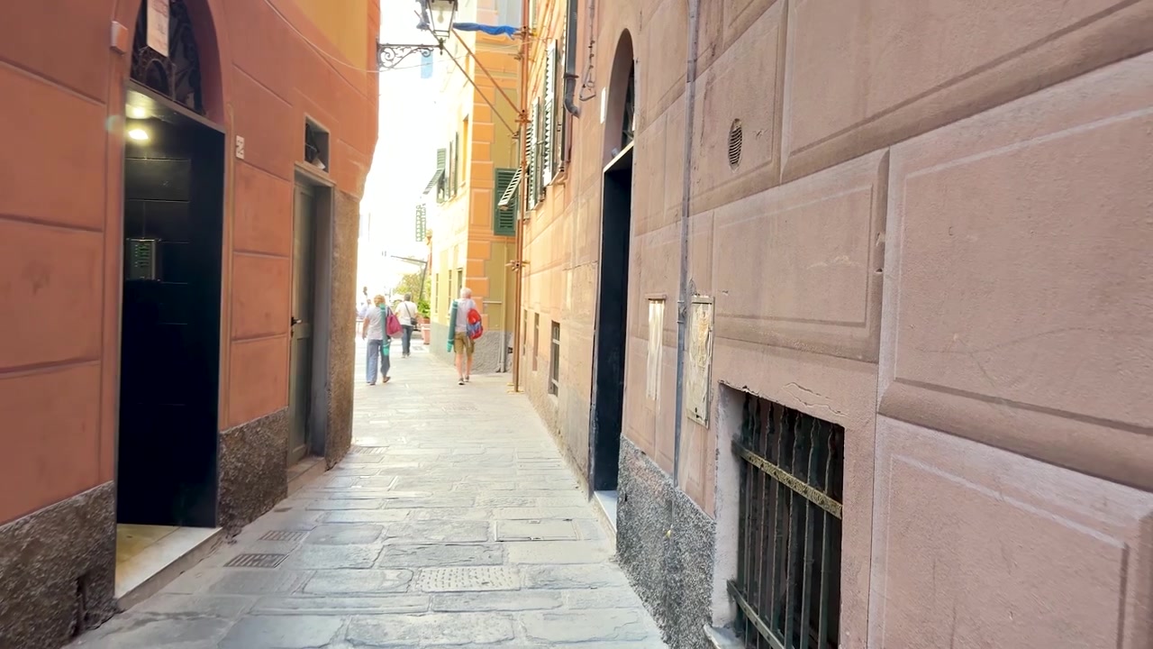 Una telecamera a mano si muove attraverso uno stretto vicolo in pietra tra colorati edifici mediterranei in Italia.