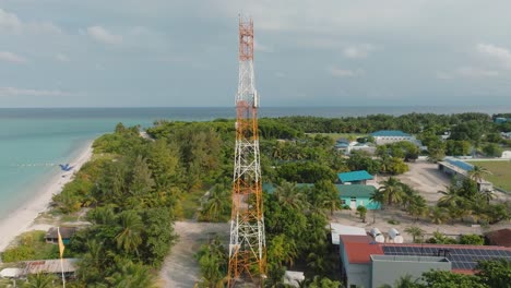 a high angle shot of a power transmitter at a coastal landscape with buildings and tropical trees