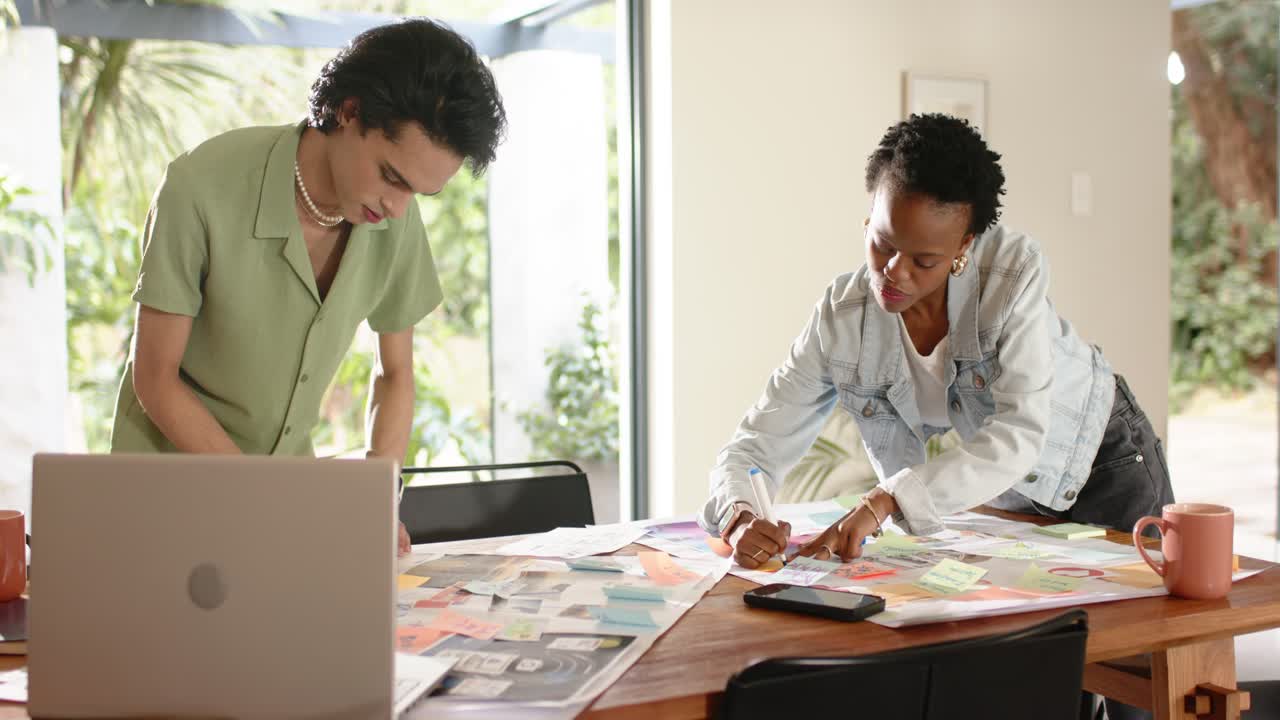 Opening with diverse coworkers leaning over table in office arranging sticky notes planning project