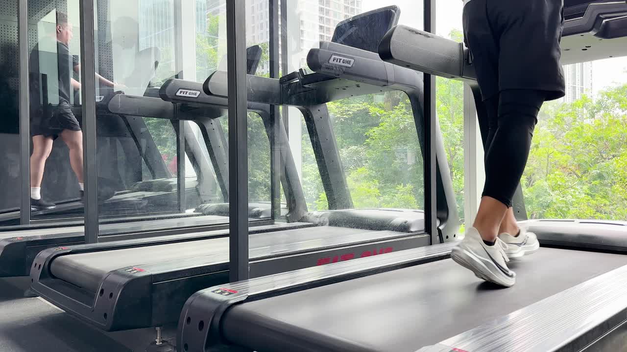 Athlete performs treadmill warm-up in bright gym with large windows, natural daylight, and steady camera