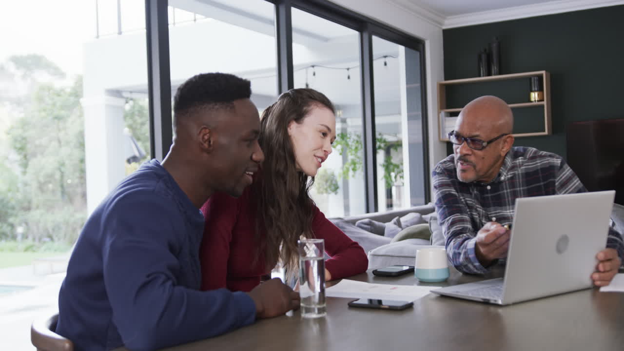 Happy diverse couple and male financial advisor using laptop and smiling at home,slow motion