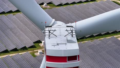 a wind turbine producing clean energy inside a solar farm - rows of solar panels seen behind the spinning blades