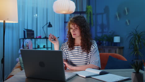 Young-woman-teacher-study-at-home-on-laptop-computer-making-conference-video-call-talking-to-webcam