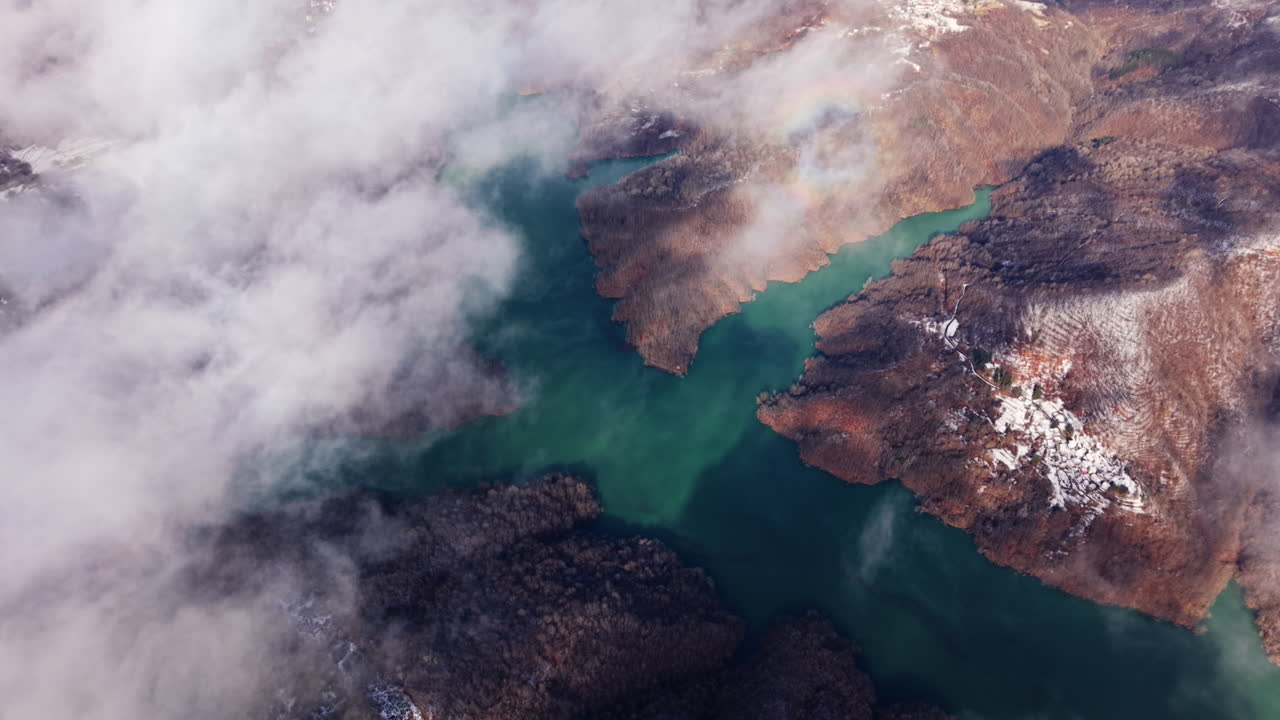 Vista aérea de paisagem montanhosa nublada sobre um lago esmeralda no inverno