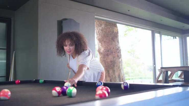 African American women smiling, leaning over pool table shooting pool for fun at home