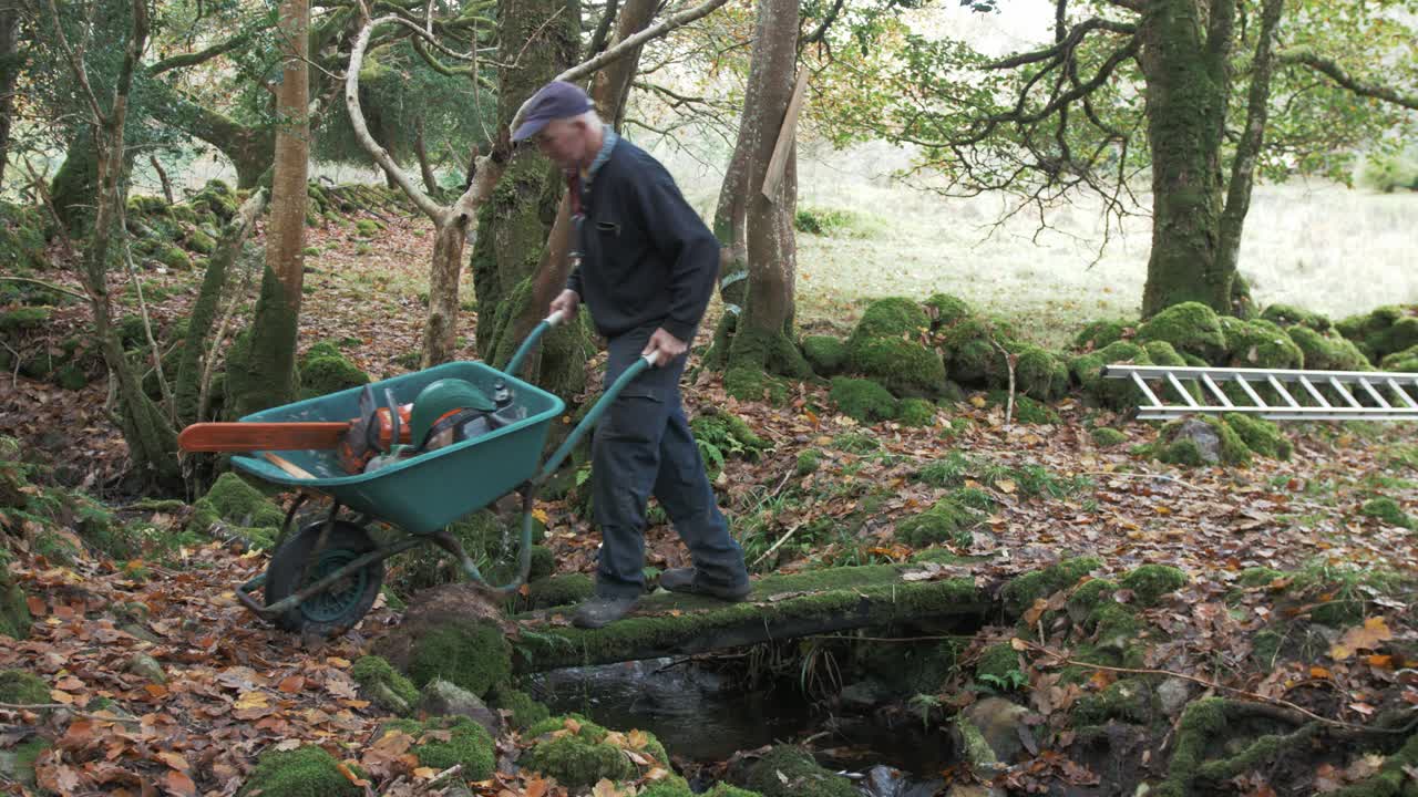 성숙한 남자는 전기톱을 실은 손수레로 개울을 건넌다
