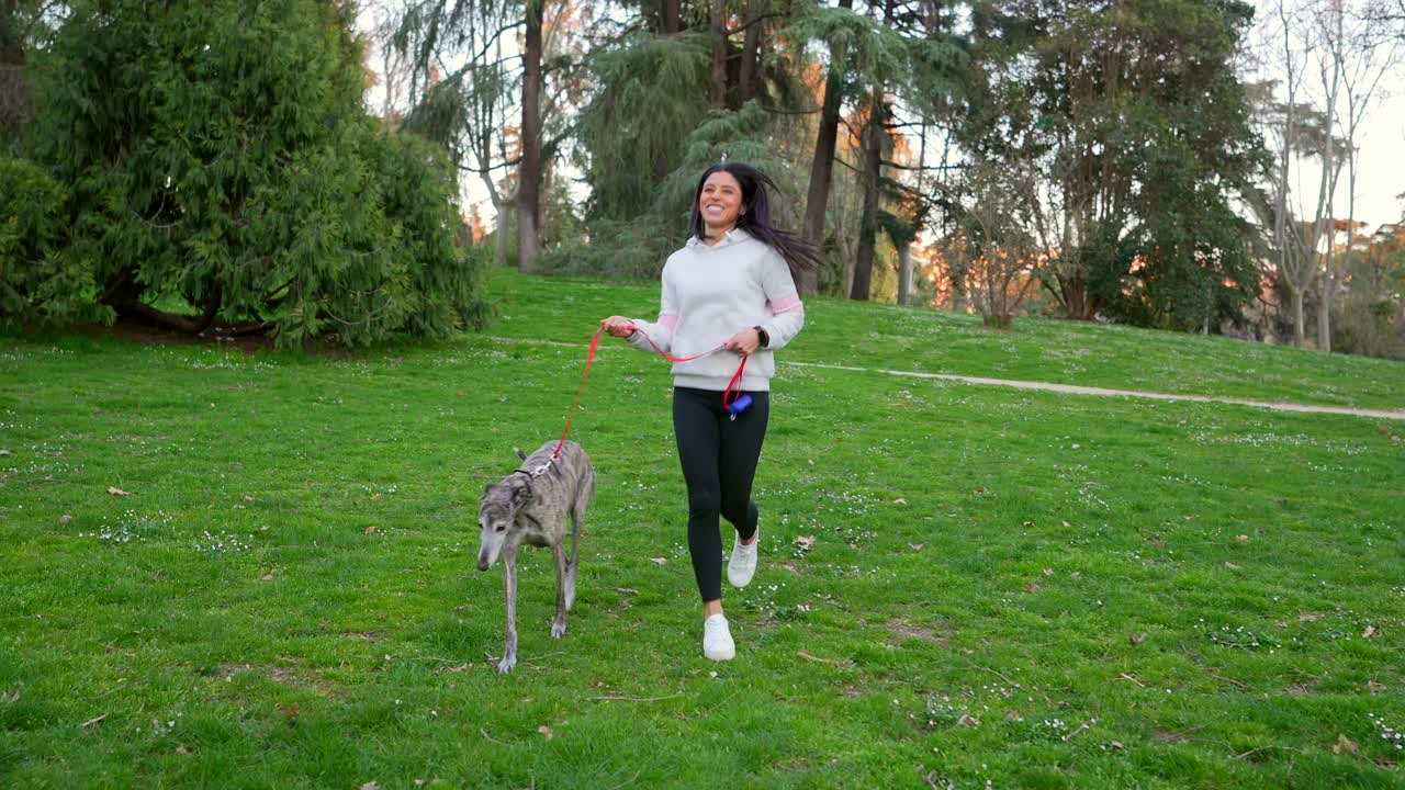 Mujer feliz paseando a su perro galgo en un parque verde