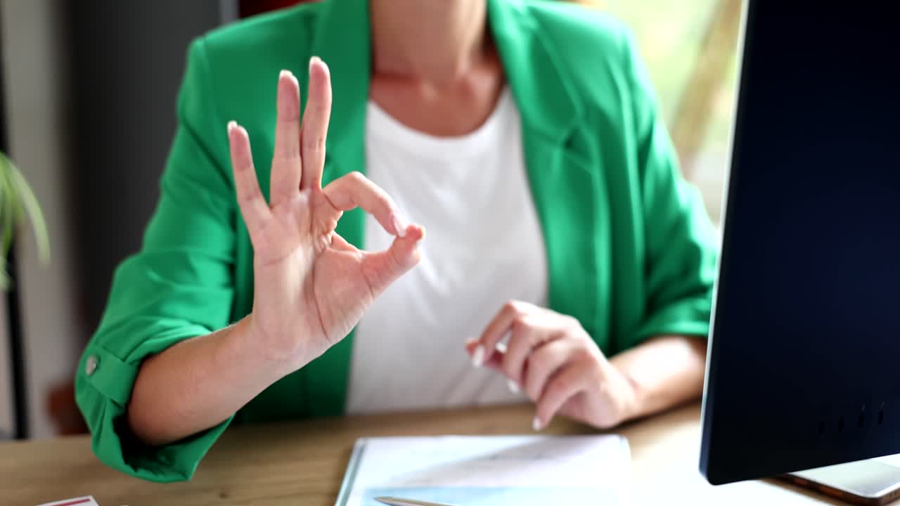Woman showing ok sign at desk in office