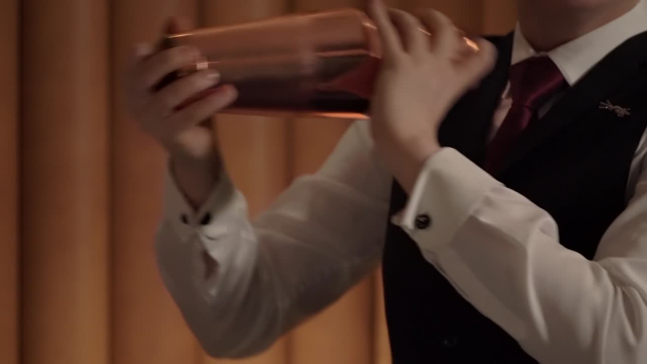 A young barmaid is shaking a fancy cocktail in a copper boston shaker.