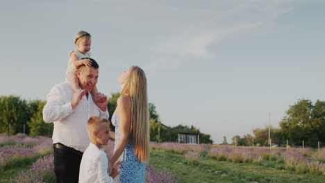 Portrait-of-a-happy-family-in-a-lavender-field,-their-house-in-the-distance.-4k-video