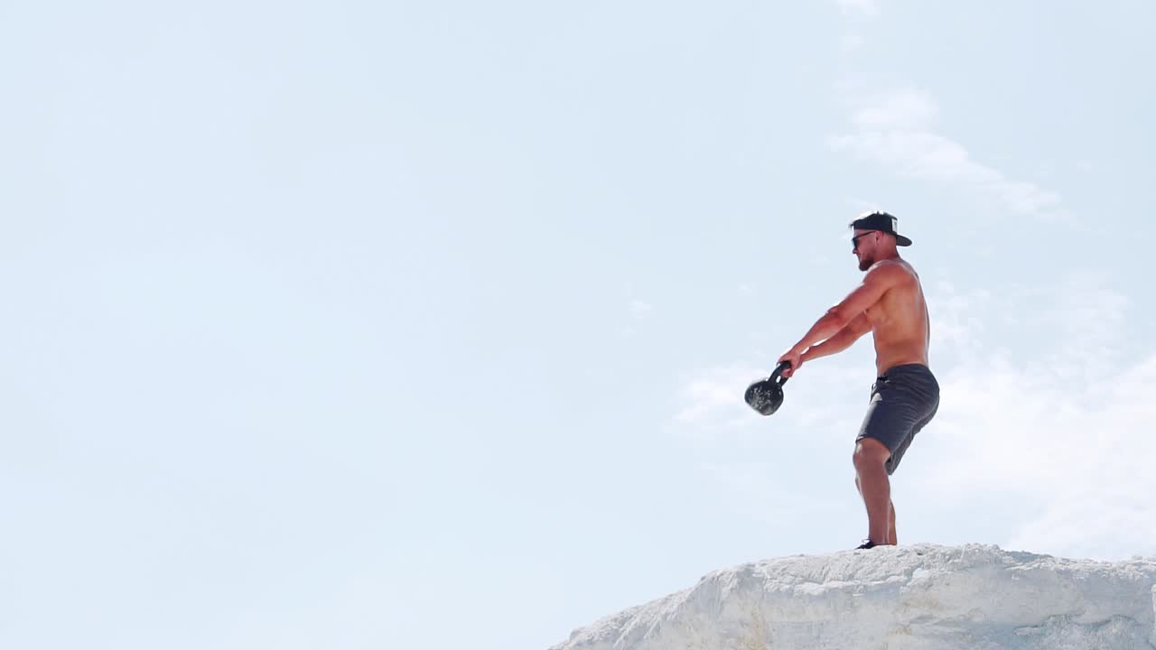 Strong man doing exercises with a kettlebell while holding her hands. Training in nature. Slow motion