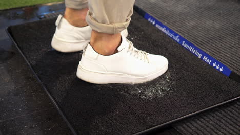 person rubs white sneakers on sanitizing mat to disinfect