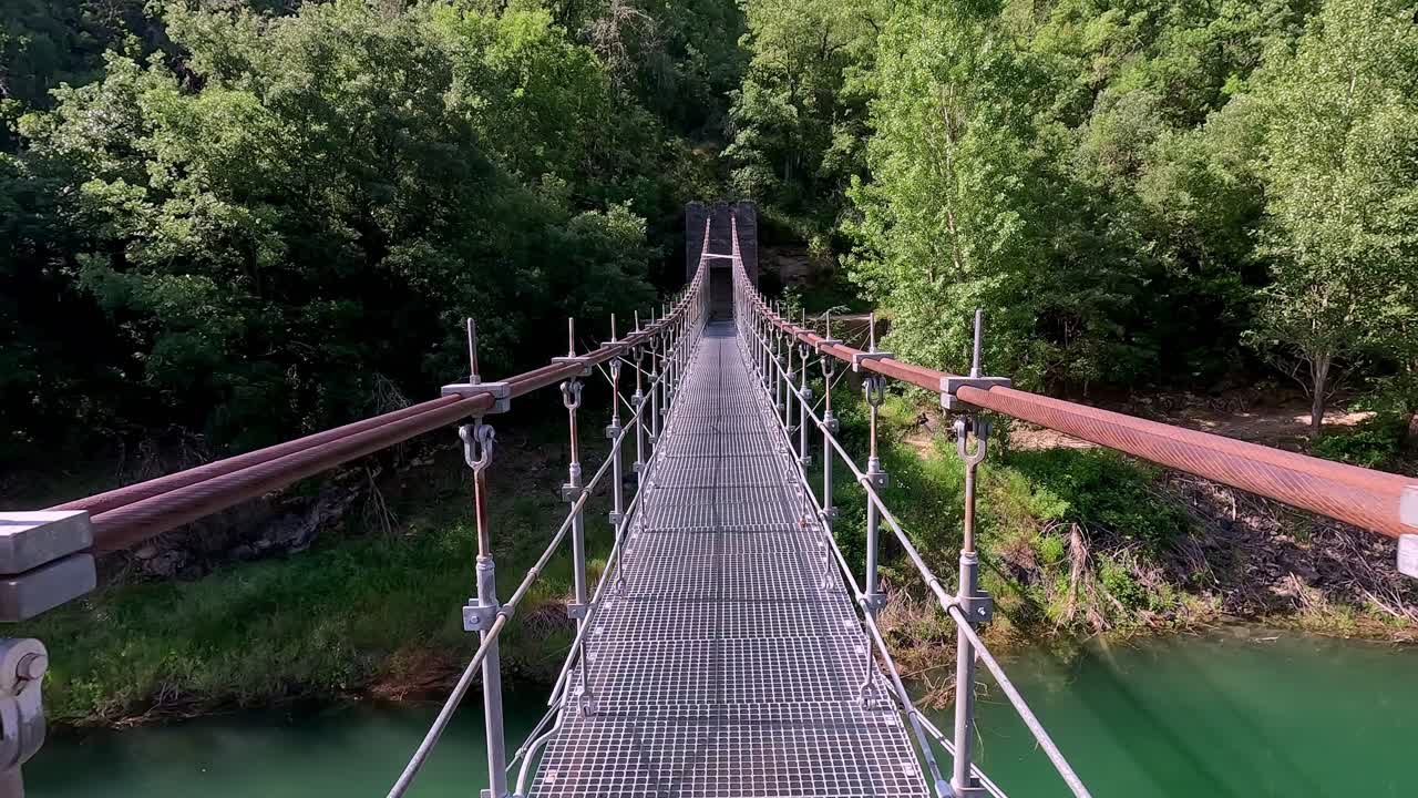 A perspective view of a suspension bridge in Congost de Mont-rebei, Catalonia, showcasing the lush greenery and clear blue skies of the picturesque natural environment.