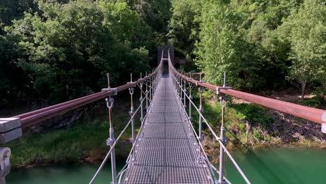 a perspective view of a suspension bridge in congost de mont-rebei, catalonia, showcasing the lush greenery and clear blue skies of the picturesque natural environment.