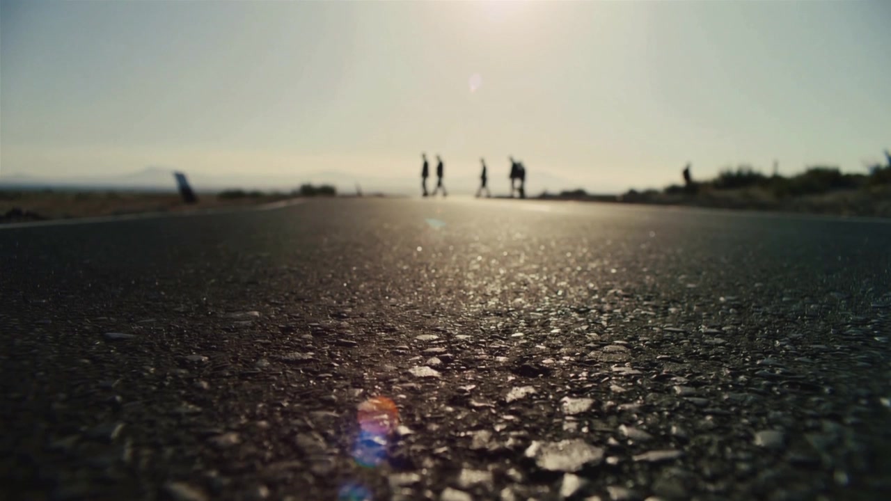 Gruppo di amici che cammina e si muove all'orizzonte su una strada asfaltata, telecamera in movimento, flare solare.