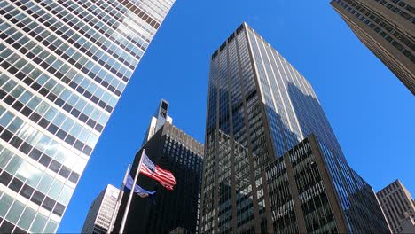 Tall-business-district-buildings-in-New-York-city-with-USA-flag-and-blue-sky-in-the-background