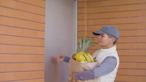 female courier with bag of fruits knocking on door of client